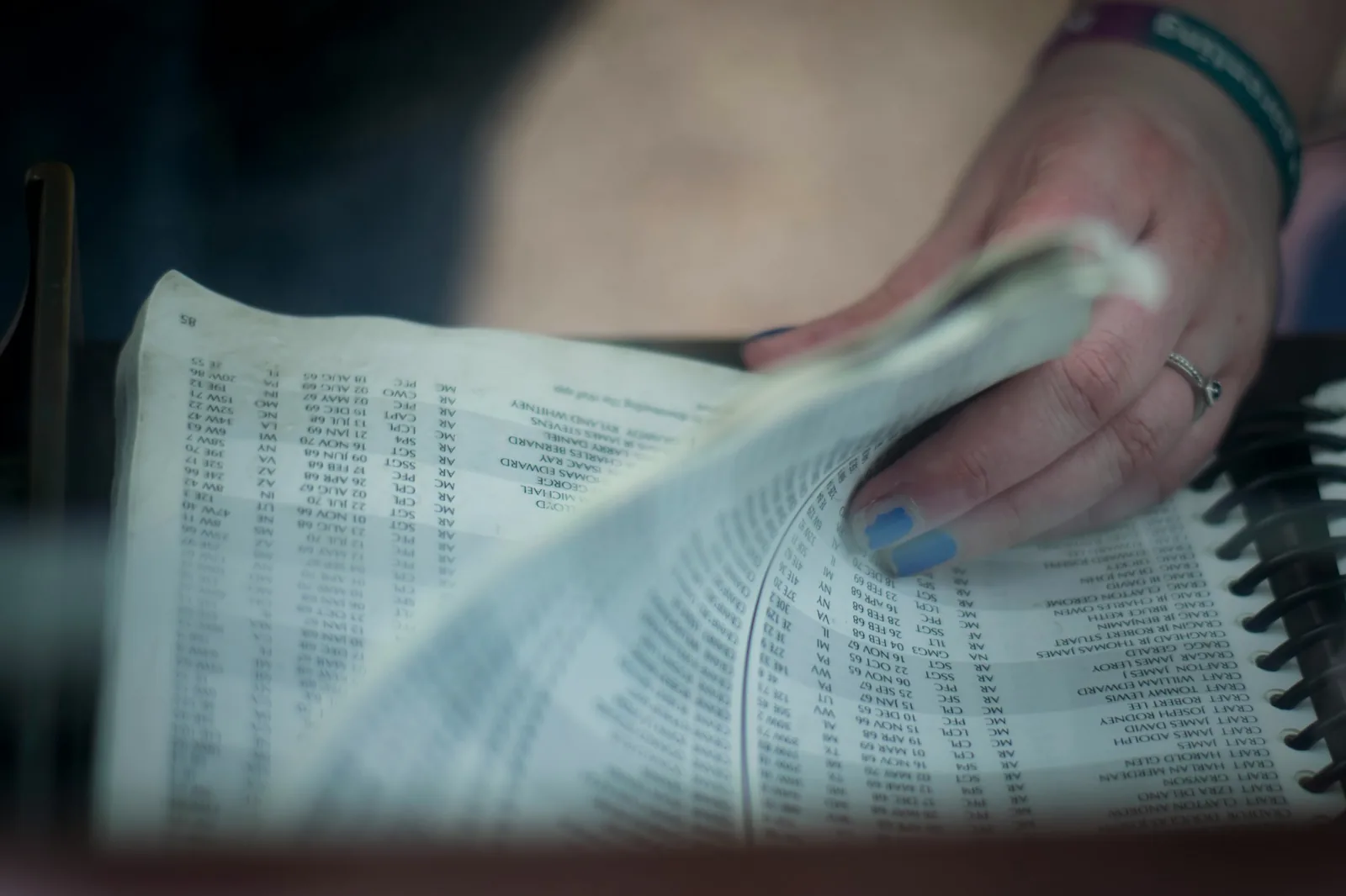 A hand flipping through the dense name columns of a printed phone book