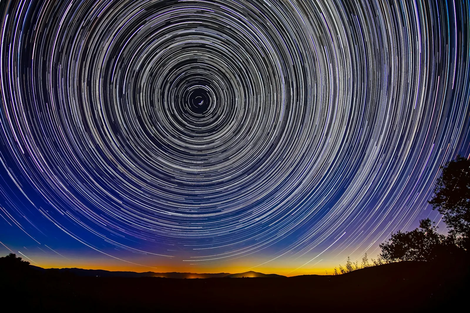 A long-exposure photograph of star trails circling the celestial pole over a dark ridgeline